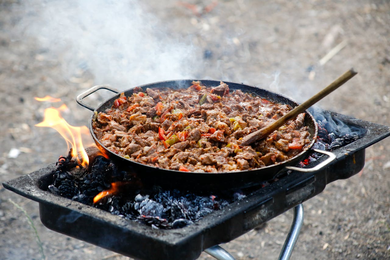 team-02 Delicious BBQ meat cooked outdoors on an open fire grill with vibrant peppers.