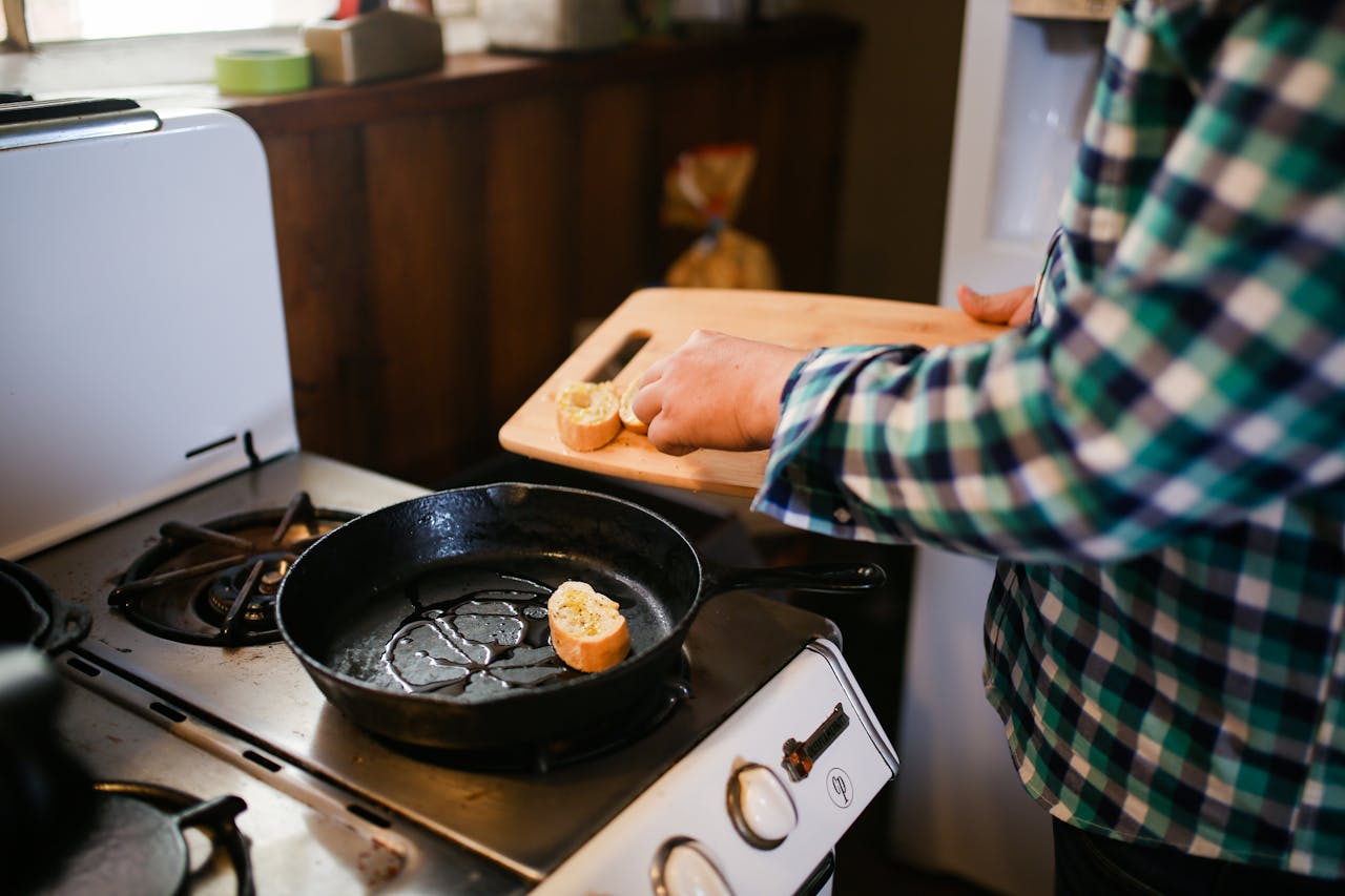 home-hero Person cooking with skillet on stove, preparing a delicious meal. Cozy kitchen atmosphere.