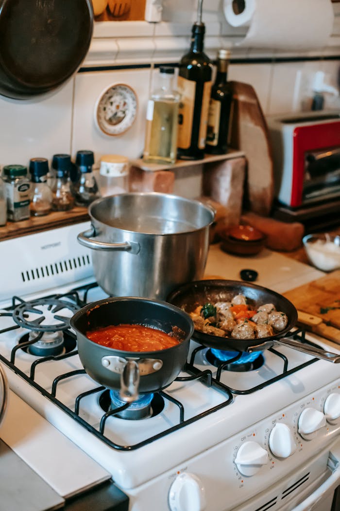 team-03 Delicious meatballs in pan between saucepans with water and salsa on gas stove in house kitchen